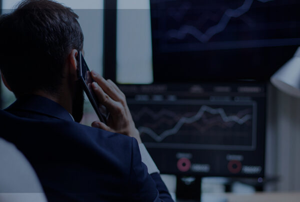 Homem sentado falando ao celular olhando um gráfico no Computador. | Qual é a importância das estratégias omnichannel?