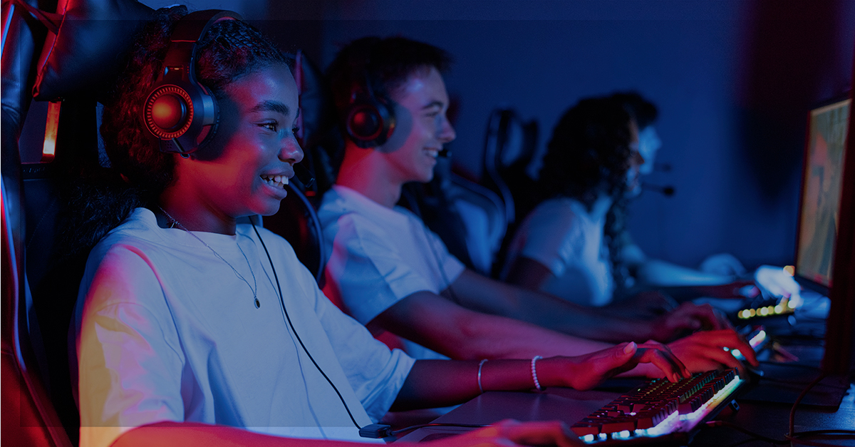 Grupo de jovens jogando em computadores em um ambiente escuro, com luzes coloridas, representando o impacto da tecnologia e telecomunicações no entretenimento.