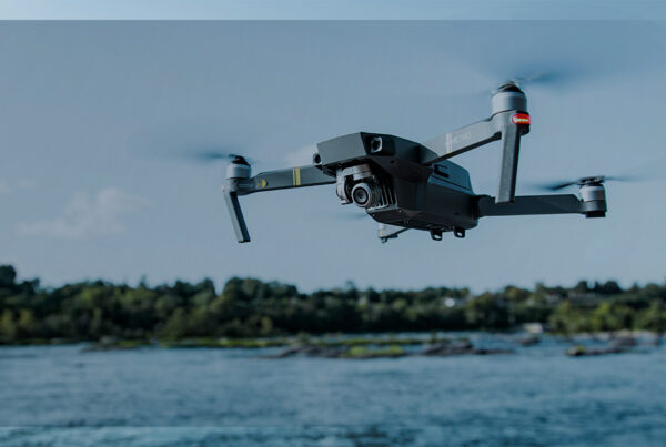 Drone voando sobre um rio com vegetação ao fundo, representando uso de tecnologia para logística e monitoramento.
