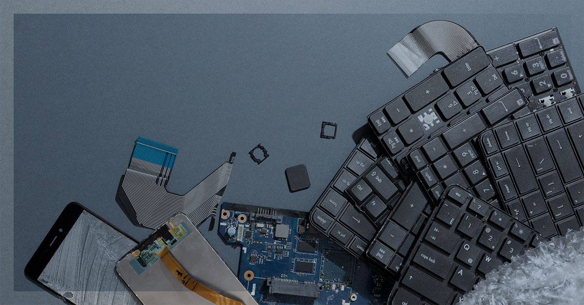Aparelhos eletrônicos desmontados e quebrados, incluindo teclado, placa-mãe, tela de celular e cabos flat, simbolizando o descarte ou reciclagem de componentes eletrônicos.