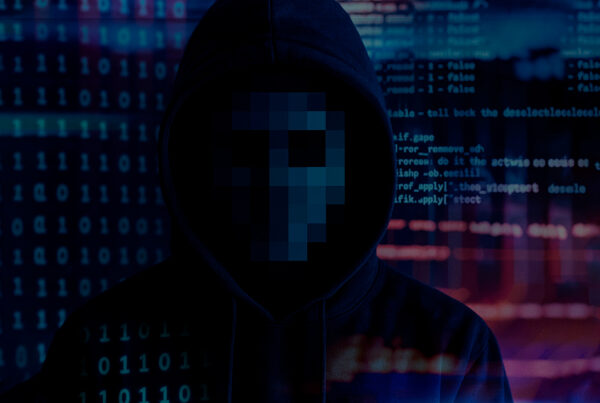 Figura com capuz em frente a um fundo de códigos binários e linguagens de programação, com o rosto pixelado para ocultar a identidade, simbolizando o hacktivismo e protestos digitais.