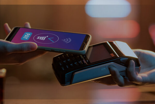 Pessoa aproximando um smartphone de uma máquina de pagamento com tecnologia de aproximação, representando o uso de carteiras digitais para transações sem contato.