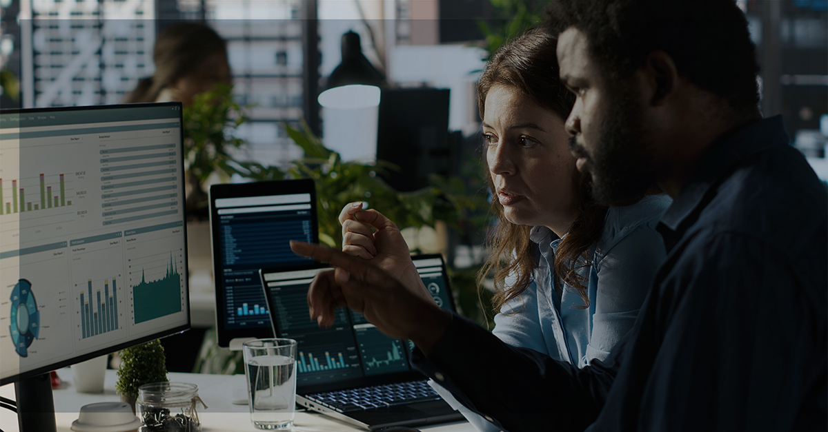 Dois analistas observam dashboards em monitores em um escritório moderno, representando a cultura de dados em pequenas e médias empresas.