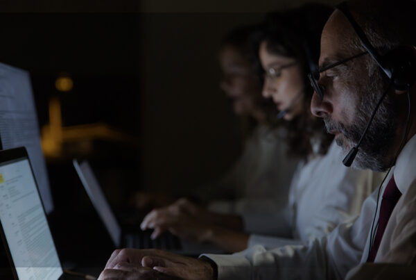 Profissionais de suporte com headsets trabalham à noite diante de notebooks, ilustrando governança de TI e operações contínuas.