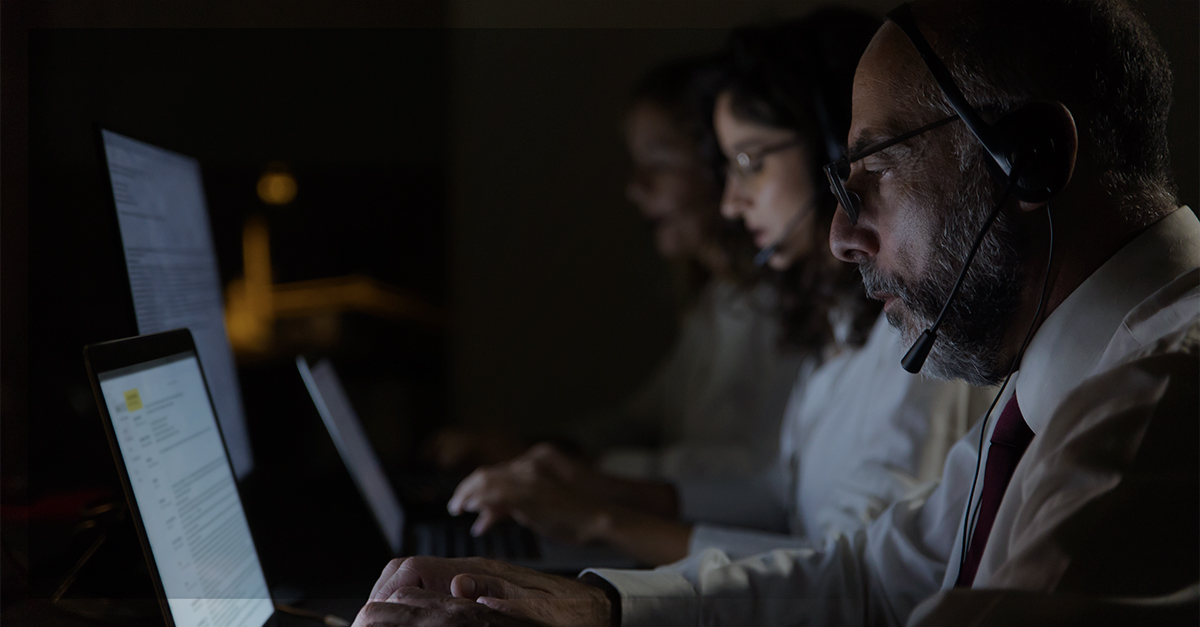 Profissionais de suporte com headsets trabalham à noite diante de notebooks, ilustrando governança de TI e operações contínuas.